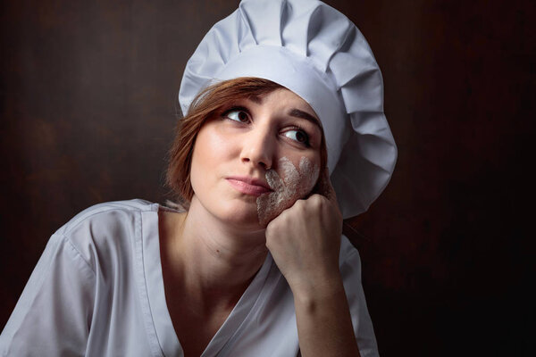 Tired young beautiful girl in a chef uniform on a brown backgroud.