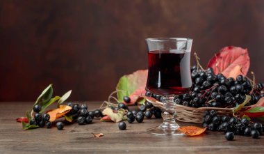 Fresh juice of ripe black chokeberry (Aronia melanocarpa) in glass and berries with leaves on wooden background. clipart
