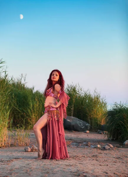 Beautiful young woman in Oriental dance costume by the sea. Expensive costume decorated with rhinestones and beads. Dancing girl on the seashore.