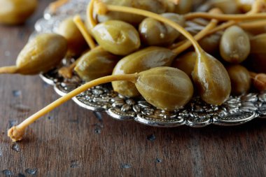 Metal tabak içinde turşu Kapari Karpuzu. Capparis yenilebilir meyve. Çilek garnitür olarak kullanılır. Eski ahşap arka plan.