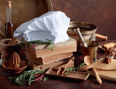 Beyaz şefin şapka ve eski yemek kitapları. Baharat ve mutfak masasında biberiye ile mutfak eşyaları.