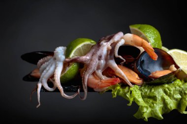 Siyah bir zemin üzerine salata ve limon dilimleri ile karışık lezzetli deniz ürünleri.