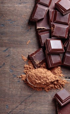 Kırık çikolata parçaları ve ahşap arka plan üzerinde küçük kaşık kakao tozu. Üstten Görünüm, kopya alanı