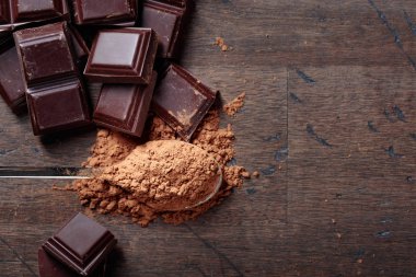 Çikolata parçaları ve eski ahşap arka plan üzerinde küçük kaşık kakao tozu. Üstten görünüm, kopya alanı.