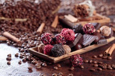 Ahşap tabak içinde çeşitli çikolatalar. Tarçın ve kahverengi bir masada kahve çekirdekleri ile tatlılar.