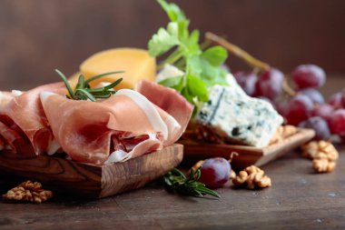 Prosciutto çeşitli peynirler, üzüm ve eski ahşap bir masa üzerinde ceviz.