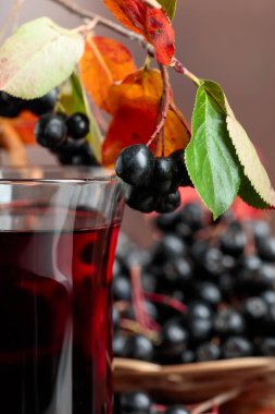 Olgun siyah chokeberry (Aronia melanocarpa) cam ve ahşap arka plan üzerinde yapraklarla meyveleri taze meyve suyu.