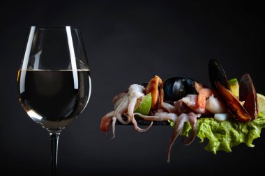 Bardak beyaz şarap, lezzetli deniz ürünleri, salata ve kireç dilimleri siyah bir zemin üzerine karışık. Metniniz için kopya alanı.