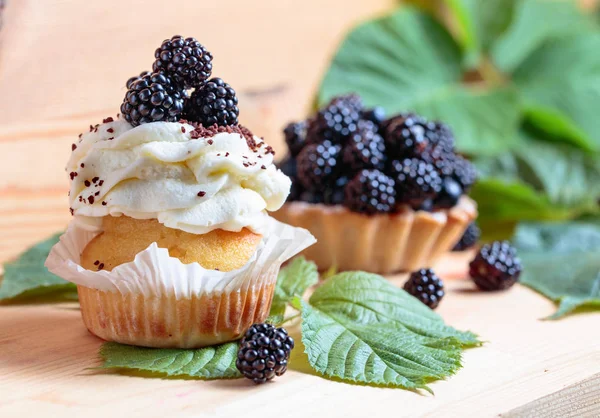 Tasty blackberry cakes with berries and cream on a wooden table.