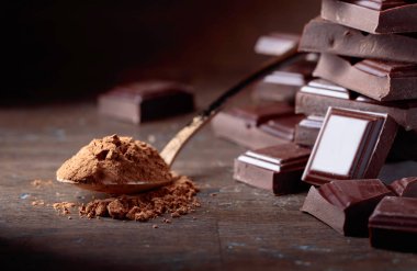 Kırık çikolata parçaları ve ahşap bir masa küçük kaşık kakao tozu.
