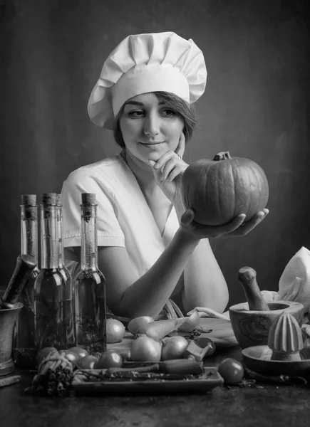 年轻漂亮的女孩在一个厨师制服与南瓜 餐桌上的各种厨具和蔬菜 — 图库照片
