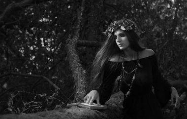 Vintage Gotik Giysi ve büyülü kitap tutan güzel genç halloween cadı. Karanlık ormanda cadı. Siyah ve beyaz.