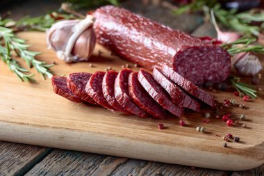 Eski ahşap bir masada tütsülenmiş salam. Biberiye, sarımsak ve biberli sosis..