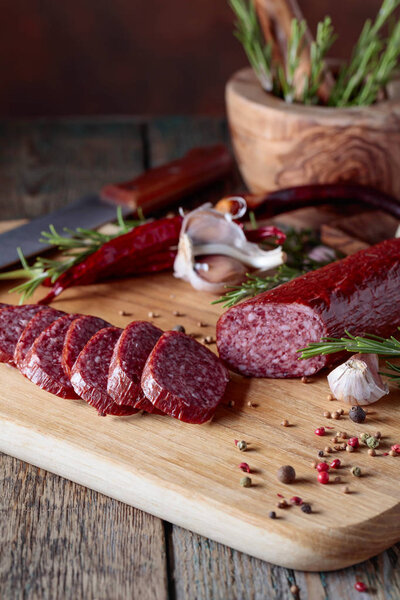 Копченая салями на старом деревянном столе. Сосиски с розмарином, чесноком и перцем.