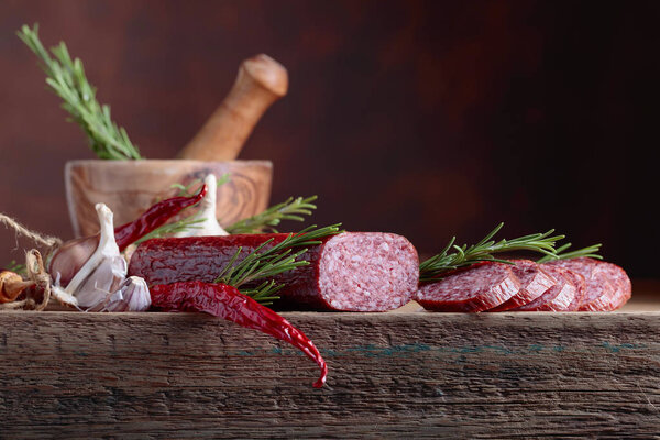 Smoked salami on a old wooden table. Sausages with rosemary , garlic and pepper. Natural wooden background. Copy space for your text.
