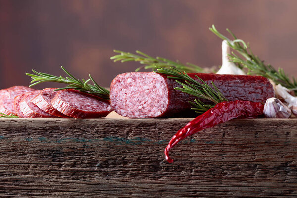 Smoked salami on a old wooden table. Sausages with rosemary , garlic and pepper. Natural wooden background. Copy space for your text.