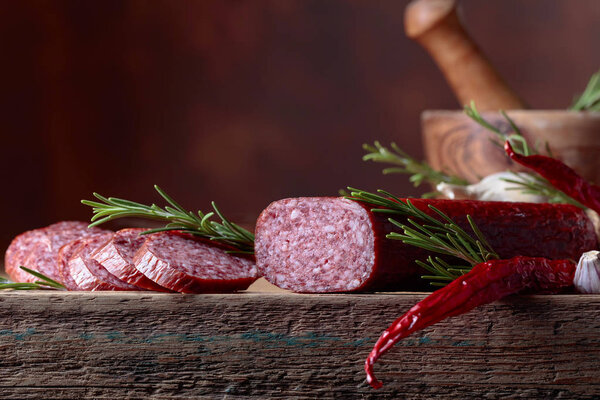 Smoked salami on a old wooden table. Sausages with rosemary and pepper. Natural wooden background. Copy space for your text.