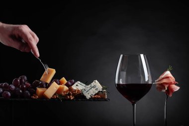 Çeşitli peynirler, meyve ve prosciutto siyah bir zemin üzerine kırmızı şarap.