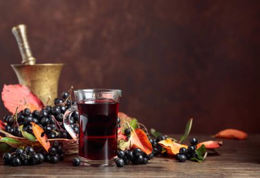 Olgun siyah chokeberry (Aronia melanocarpa) cam ve ahşap arka plan üzerinde yapraklarla meyveleri taze meyve suyu.