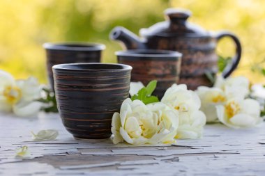 Seramik bardak, Çaydanlık ve beyaz köpek gül bahçesinde eski ahşap bir masa üzerinde. Yabani gül ile aromatik ve canlandırıcı çay.