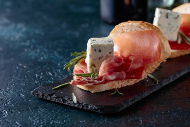 Jambon, mavi peynir ve karanlık bir arka plan üzerinde biberiye ile sandviç. 