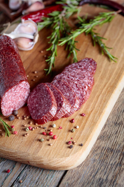 Копченая салями на старом деревянном столе. Сосиски с розмарином, чесноком и перцем.