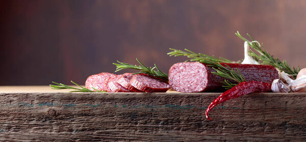 Smoked salami on a old wooden table. Sausages with rosemary , garlic and pepper. Natural wooden background. Copy space for your text.