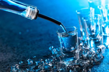 Votka ile mavi arka plan ışığı yaktı bir bardak içine dökülür. Uzay kopyalayın. Adet buz ile soğuk votka.