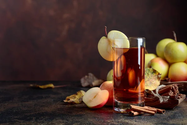 Bardak elma suyu veya elma suyu ile sulu elma ve tarçın bir mutfak masasında.