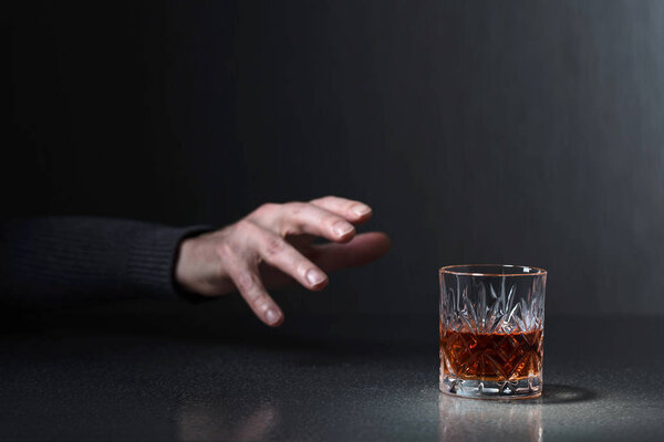 Man's hand reaches for a glass of alcohol. Conceptual image on the subject of alcoholism. Copy space for your text.