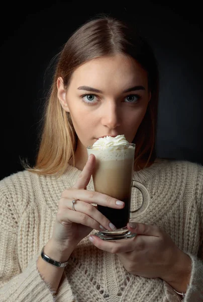 Attractive young woman with Irish coffee. Beautiful blonde in a sweater holding a mug of coffee with cream.