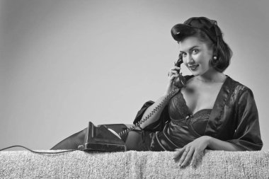 PIN tarzında vintage telefonla konuşan güzel esmer kadın. Çekici genç kadın 50s tarzı mükemmel makyaj ve saç modeli ile. Siyah ve beyaz.
