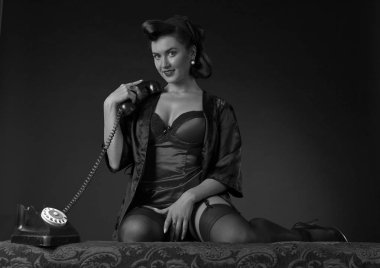 PIN tarzında vintage telefonla konuşan güzel esmer kadın. Çekici genç kadın 50s tarzı mükemmel makyaj ve saç modeli ile. Siyah ve beyaz.