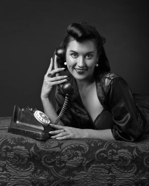 PIN tarzında vintage telefonla konuşan güzel esmer kadın. Çekici genç kadın 50s tarzı mükemmel makyaj ve saç modeli ile. Siyah ve beyaz.