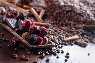 Ahşap tabak içinde çeşitli çikolatalar. Tarçın ve kahverengi bir masada kahve çekirdekleri ile tatlılar.