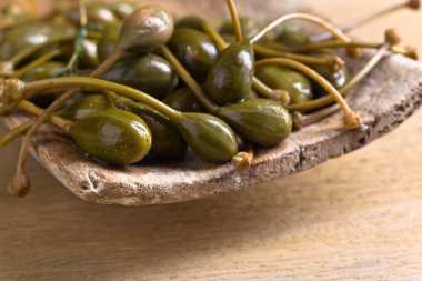 Mutfak masasının üzerinde ahşap tabak içinde konserve Kapari .