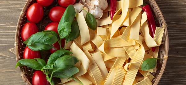 Uncooked Italian noodles with garlic, basil, tomatoes cherry and red chili pepper. Top view.