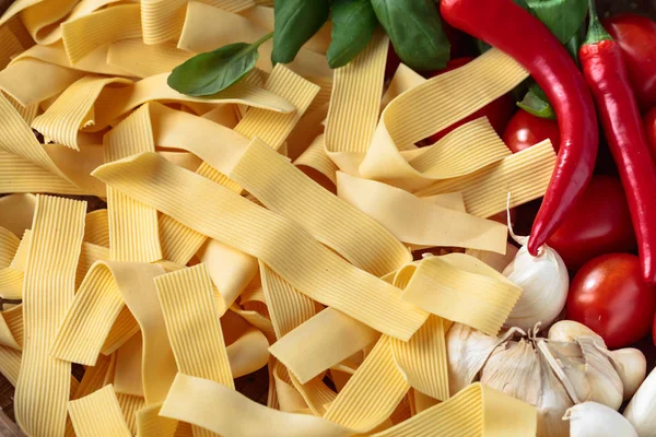 Uncooked Italian noodles with garlic, basil, tomatoes cherry and red chili pepper.