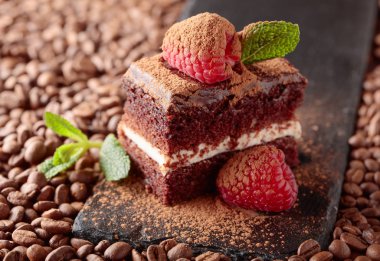 Çikolatalı kek ahududu ve naneli kahve çekirdekleri ile bir tabloda closeup. Kakao tozu ile serpilir. 