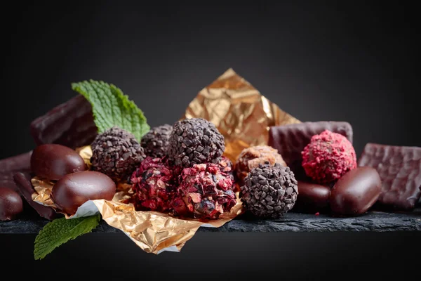 Various chocolates with mint leaves on a black background. Copy space.