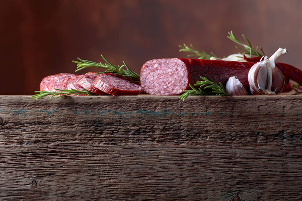 Smoked salami on a old wooden table. Sausages with rosemary and garlic. Natural wooden background. Copy space for your text.