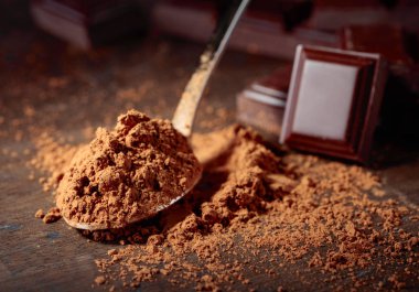 Kırık çikolata parçaları ve ahşap arka plan üzerinde küçük kaşık kakao tozu.