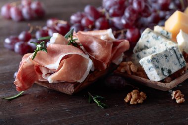 Prosciutto çeşitli peynirler, üzüm ve eski ahşap bir masa üzerinde ceviz.