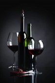 Sklenice a láhve červeného vína s vývrtkou na černém pozadí reflexní.