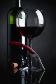 Sklo a láhev červeného vína s vývrtkou na černém pozadí reflexní.