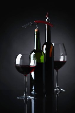 Gözlük ve tirbuşon yansıtıcı siyah bir arka plan ile kırmızı şarap şişeleri.