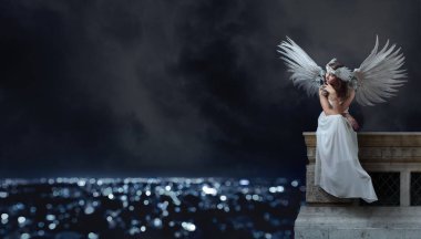 Çatıda oturan ve gece city adlı seyir Melek kanatlı beyaz elbiseli Genç güzel kadın. Güzel profesyonel makyaj, mükemmel saç, doğal tüyler ve rhinestones headdress. Kopya alanı.