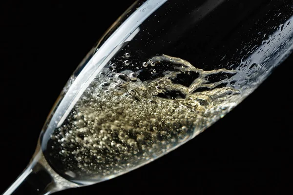 Glass of splashing champagne isolated on black background.