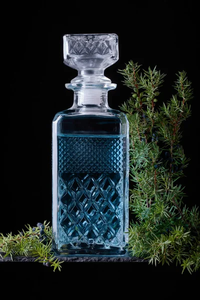 Crystal sürahi ve ardıç daldaki meyveleri siyah bir arka plan ile mavi cin.