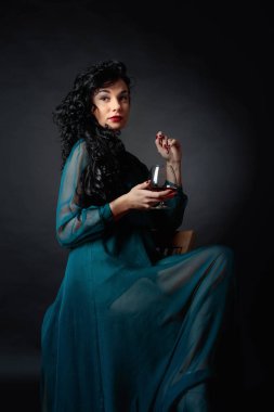 Gece elbisesi içinde uzun kıvırcık saçlı Genç güzel kadın. Uzun Abiye bardak brendi ile çekici esmer portresi.